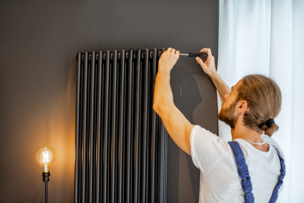 handyman setting black radiator on wall 